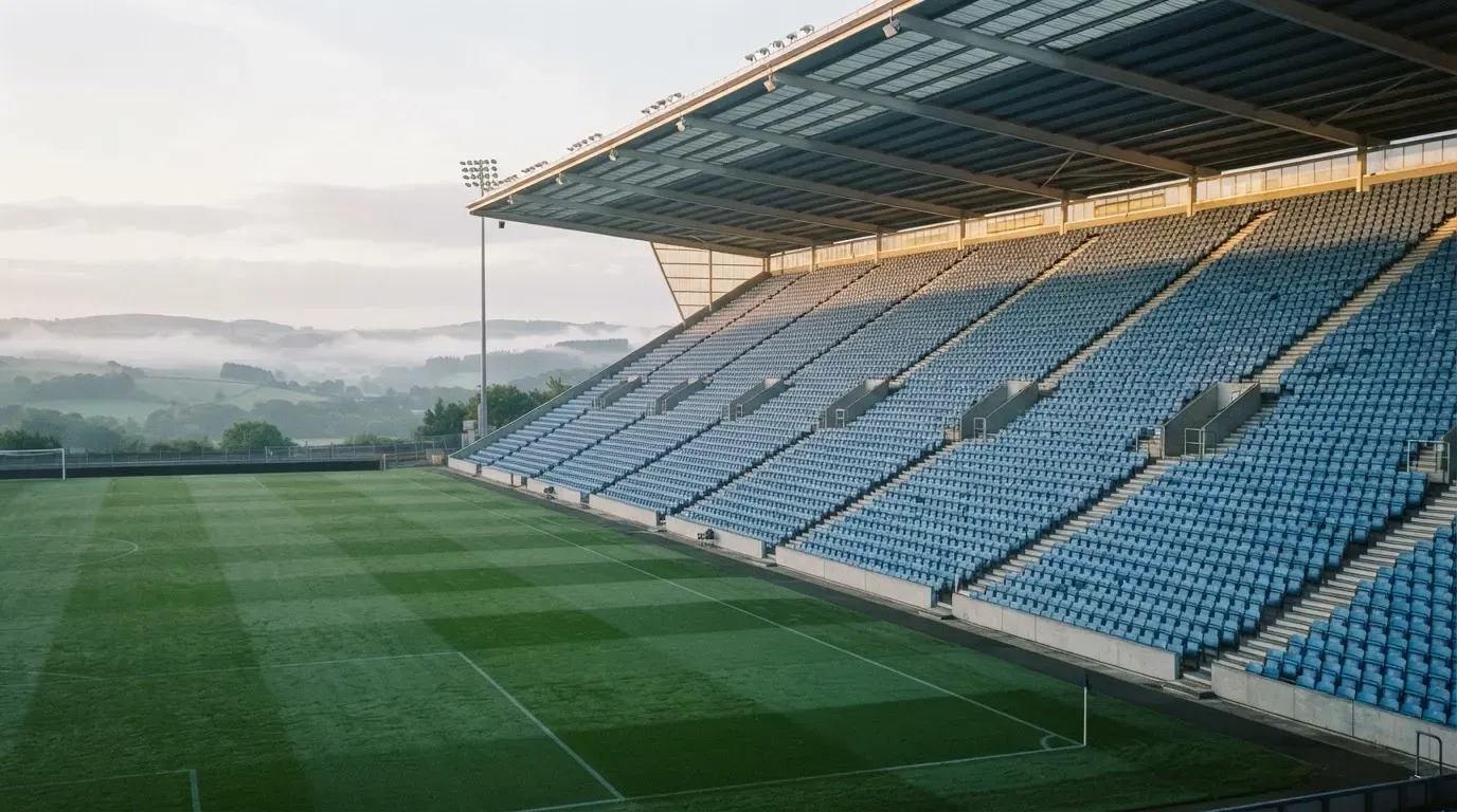 Ein leeres Stadion im Morgenlicht mit Blick auf die Sitzreihen, im Hintergrund Hügel und aufsteigender Nebel.