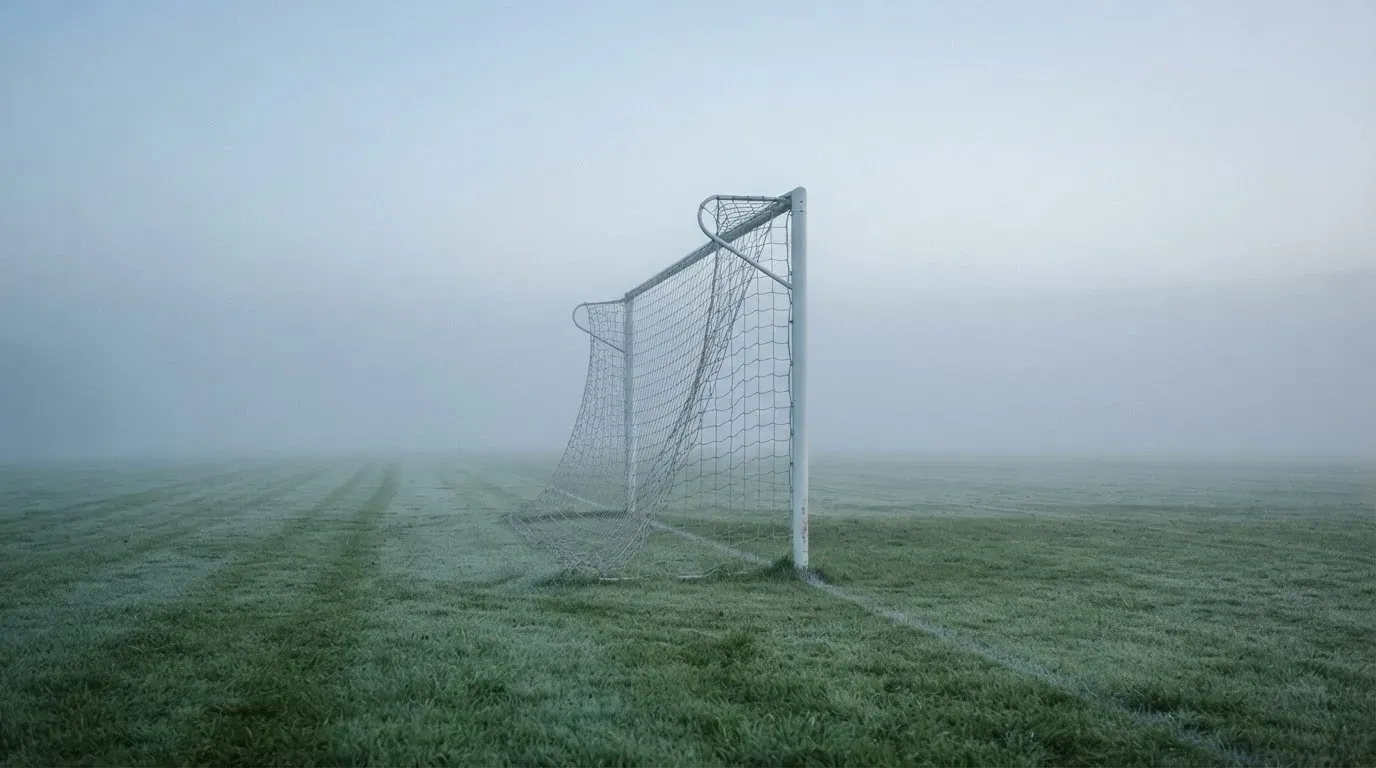 Eine Torlinie mit Netz steht am frühen Morgen im dichten Nebel auf einem Rasenplatz, die Umrisse der Pfosten verschwimmen.