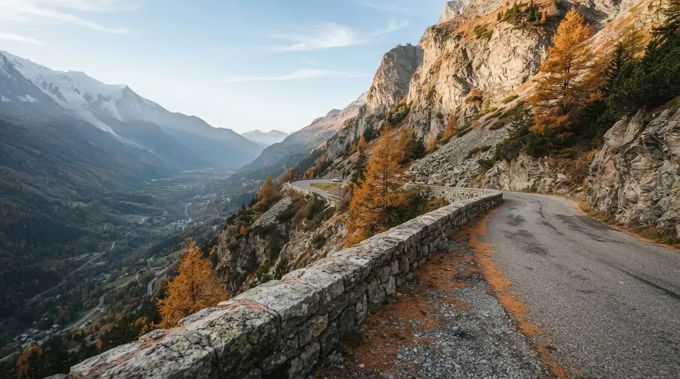 Eine Passstrasse im Hochgebirge säumt eine niedrige Steinmauer, dahinter ragen Felswände auf und der Herbsthimmel ist klar.