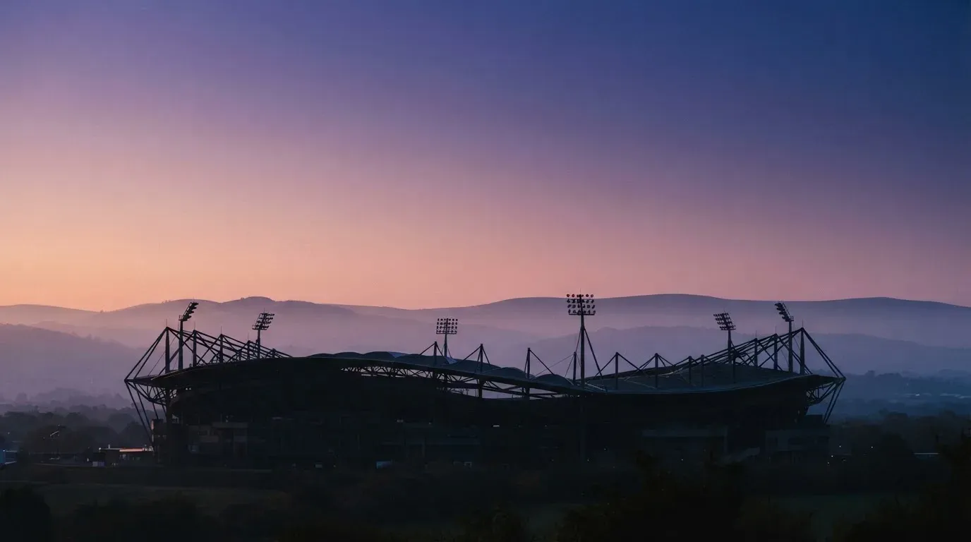 Die Silhouette eines Stadiondachs vor dem violetten Abendhimmel, dahinter eine Hügelkette.