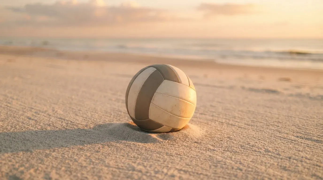 Ein Volleyball liegt auf feinem Sand an einem leeren Strand bei Sonnenaufgang.