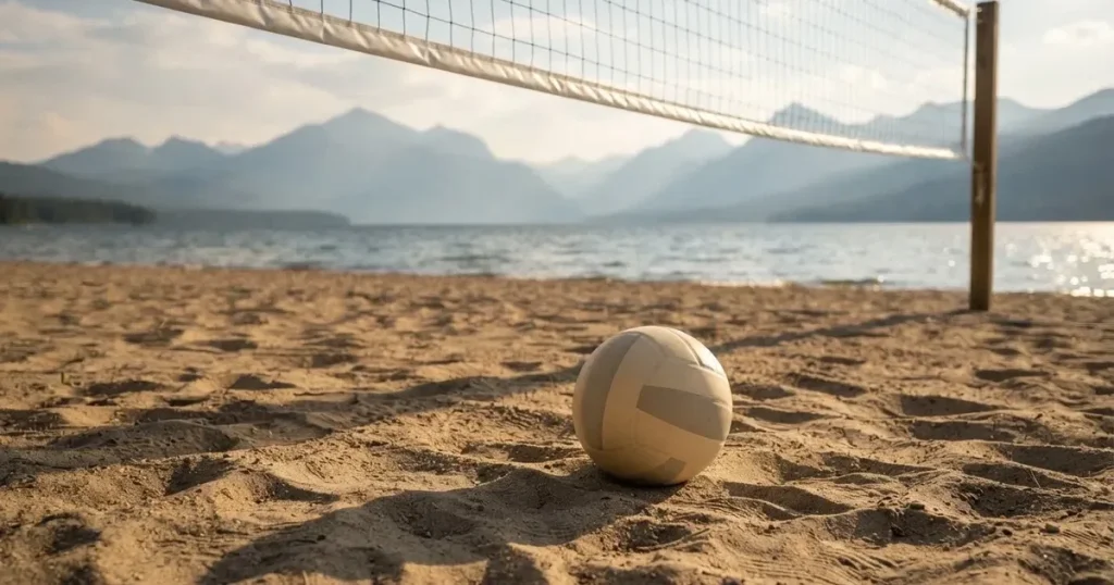 Ein Volleyball liegt am Fuss des Netzes auf Sand, im Hintergrund glitzert ein See und ein Bergzug steht im Dunst.
