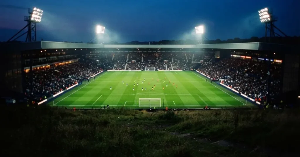 Ein Fussballstadion bei Flutlicht von einer Anhöhe aus gesehen, der Rasen leuchtet grün unter dunklem Abendhimmel