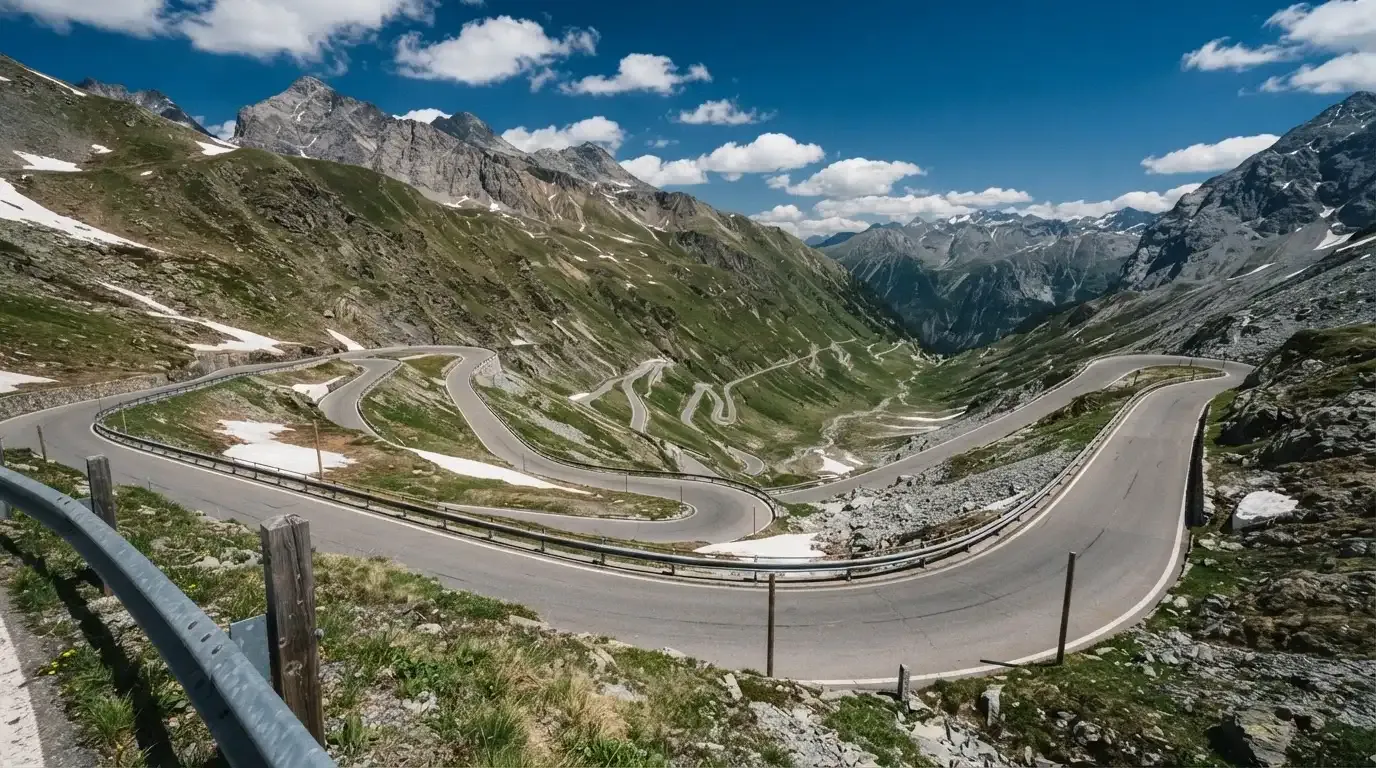 Eine Passstrasse mit Leitplanke windet sich an einem klaren Tag durch eine Berglandschaft.