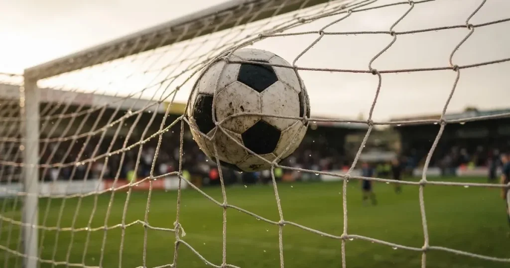 Ein Fussballnetz in Nahaufnahme, in dem ein Ball hängt, Wassertropfen glänzen auf den Maschen.
