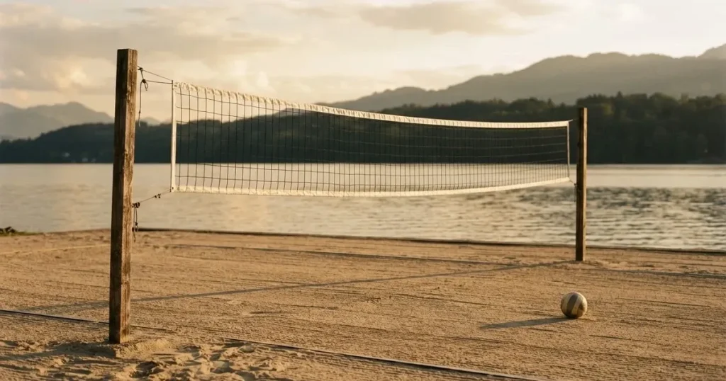Ein Volleyballnetz am Sandstrand eines Sees, späte Nachmittagssonne, das Wasser liegt glatt im Hintergrund