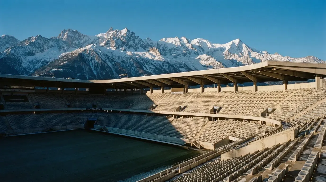 Schneebedeckte Berggipfel erheben sich im klaren Morgenlicht hinter einem leeren Stadion mit hellen Zuschauerrängen.