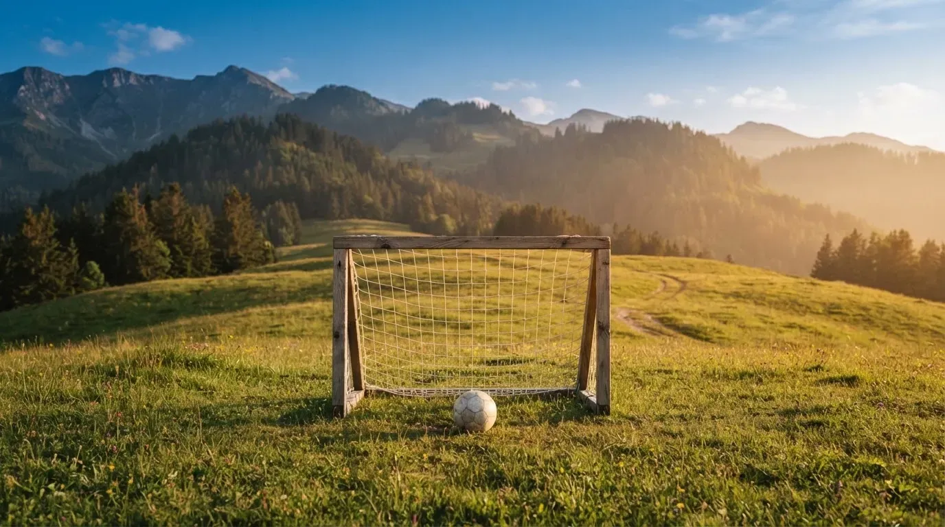 Eine Almwiese mit einem kleinen Holztor für Kinderfussball, dahinter erheben sich bewaldete Hänge im Nachmittagslicht.