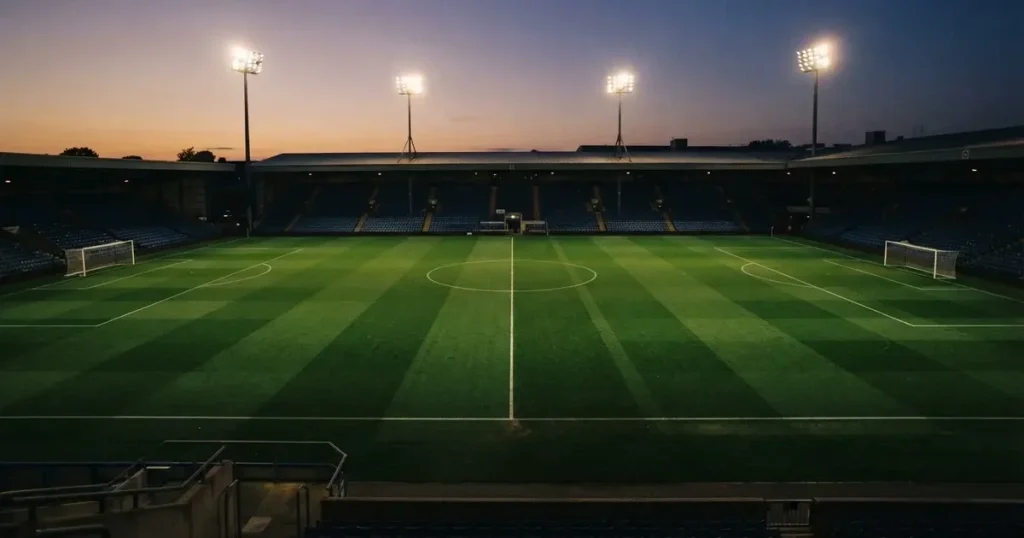 Ein menschenleerer Fussballplatz mit frisch gemähtem Rasen unter Flutlichtmasten in der Abenddämmerung, aus erhöhter Perspektive fotografiert.