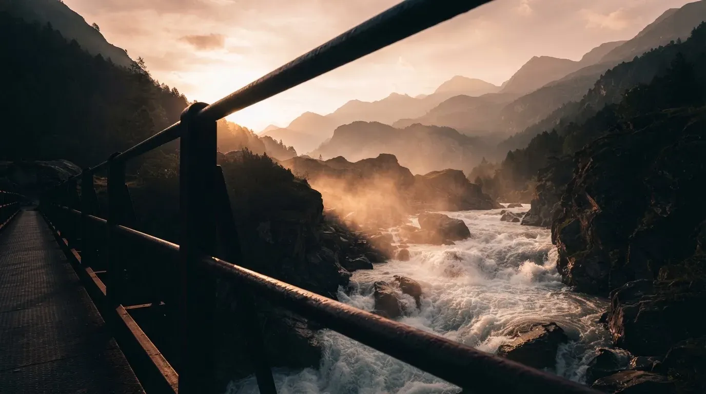Ein Brückengeländer aus Stahl über einem Gebirgsfluss im Gegenlicht, darunter schäumendes Wasser.